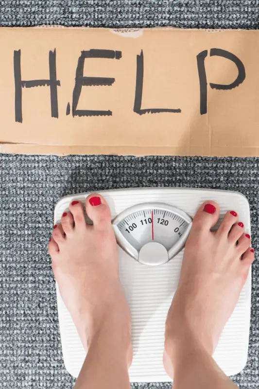 Frauenfüße auf einer Waage mit "Help"-Schild